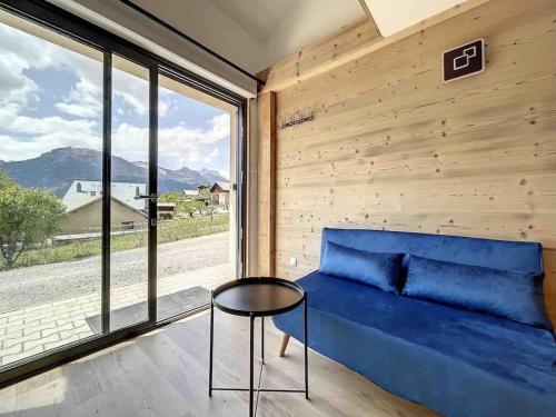 a blue couch in a room with a large window at Petit loft chaleureux et cosy - vue montagne in Guillestre