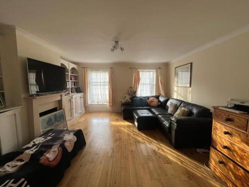 a living room with a black couch and a tv at Rooms close to Wimbledon tennis in London