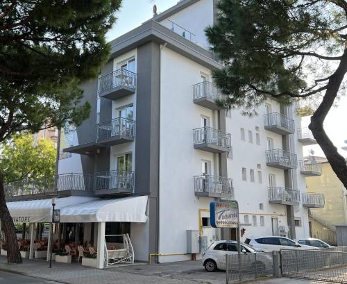 a white building with balconies and a car parked in front at Hotel Trovatore in Lido di Jesolo