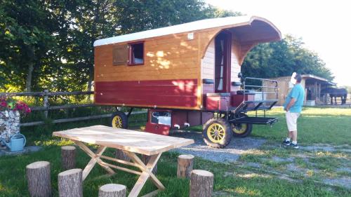 a man standing next to a wooden trailer at Véritable roulotte hippomobile "LA BAILLEUL" in Mentheville