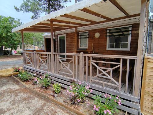a wooden cabin with a porch with flowers in front at Mobil home 6 Personnes au Atlantic Club Montalivet in Vendays-Montalivet