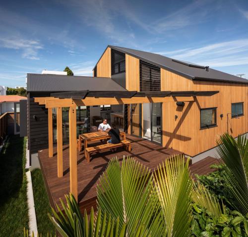 a man sitting on a deck in front of a house at Twin Peaks Beach House - New Plymouth Holiday Home in New Plymouth