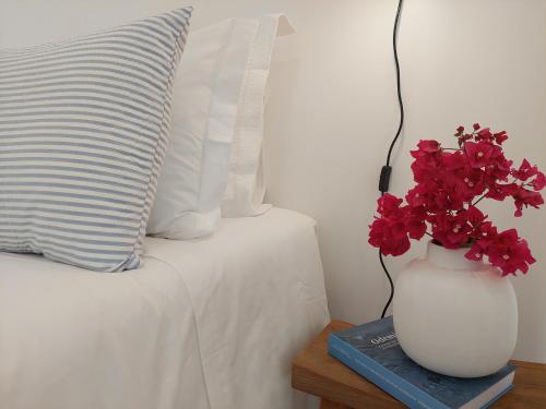 a vase with red flowers on a table next to a bed at Estúdio Lagoa Azul in Vila Nova de Milfontes