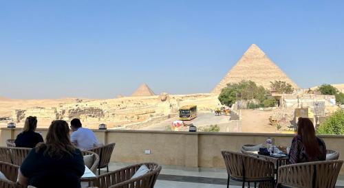 een groep mensen die aan tafels zitten en naar de piramiden kijken bij The Gate Hotel Front Pyramids & Sphinx View in Caïro