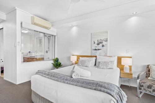 a white bedroom with a large bed and a chair at Serenity Views in Airlie Beach