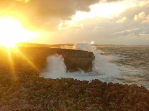 a wave hitting a cliff in the ocean at sunset at Boathouse La Bougainvillea cottage in Governorʼs Harbour