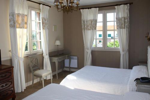 a bedroom with a bed and a desk and two windows at Hotel des Pins in Soulac-sur-Mer