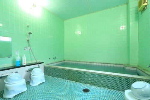 Un baño verde con bañera y dos inodoros. en Suikoen, en Yonago