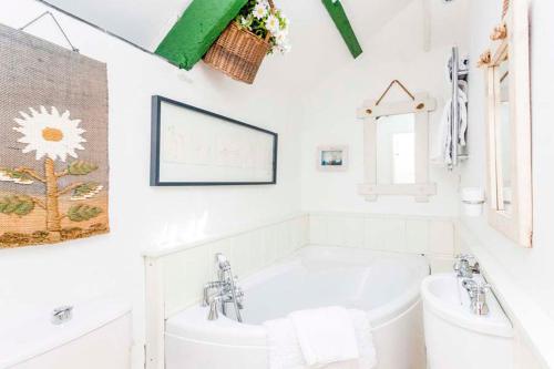 a white bathroom with a tub and a sink at Castaways, Cottage With Sea Views, Lush Gardens & Patio By the Beach in Sennen