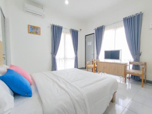 a bedroom with a white bed with blue curtains at RedDoorz at Batutulis Bogor Villa Papatong by M in Bogor