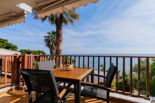 una mesa de madera y sillas en un balcón con una palmera en Amphitriti SeaFront Apartments, Loutra Agia Paraskevi en Agia Paraskevi
