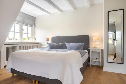 a white bedroom with a large bed and a mirror at Tortuga in Keitum