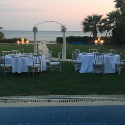 a table with white tables and chairs next to a pool at Ionion Beachfront Villa in Ayia Napa