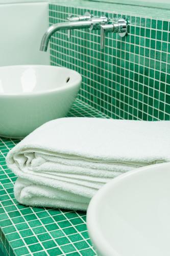 a green tiled bathroom with towels and a sink at Le Manoir du Lys, The Originals Relais in Bagnoles de l'Orne