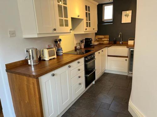 a kitchen with white cabinets and a wooden counter top at Dene Cottage in Stanton in Peak
