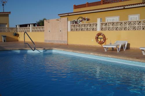 una piscina di fronte a un edificio giallo con spaghetti da piscina di Villa Ghìo a Caleta De Fuste