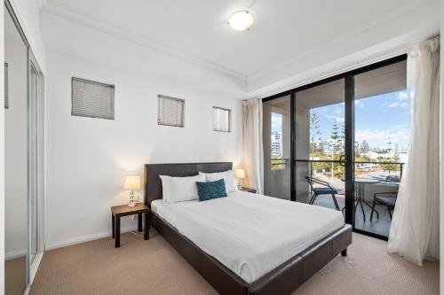 a white bedroom with a bed and a balcony at Dolphin Quay Apartments in Mandurah