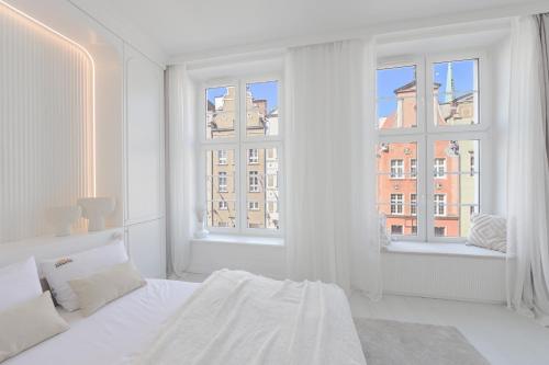 a white bedroom with a bed and two windows at Downtown Apartments Old Town Pure White in Gdańsk