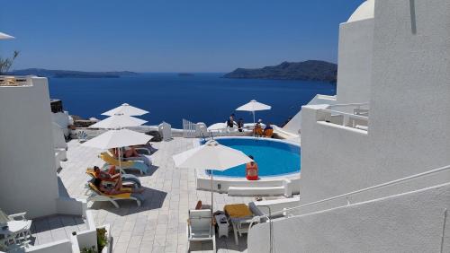 a pool with white umbrellas and chairs and the ocean at Olympic Villas in Oia