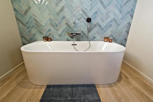 y baño con bañera blanca y pared de azulejos. en Les Petits Sablens 
