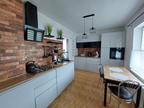 uma cozinha com armários brancos, uma mesa e uma parede de tijolos em Pokoje gościnne Na Klifie em Jastrzebia Gora