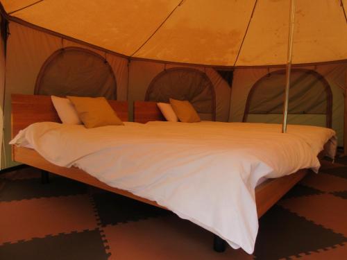 a bed in a tent with white sheets and orange pillows at DogrunCafe & Resorts JENNIE West-Karuizawa in Miyota