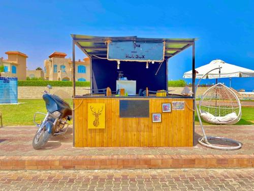a motorcycle parked in front of a wooden stand with a food cart at 50% Off. 2BR , 2BR Ground floor with pool view, private beach access, security 24/7 شاليه ٢ غرفه ، ٢ حمام ف الدور الارضي قدام جنينه و حمام السباحه مباشره ، شاطيء خاص بالقرية و أمن ٢٤ ساعه و مسجد خاص in Dawwār Muḩammad Abū Shanab