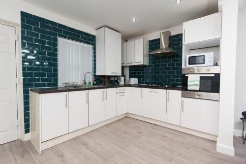 a kitchen with white cabinets and green tiles at Fewston House in Leeds