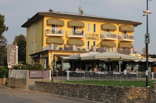 un edificio amarillo con gente sentada fuera de él en Hotel Campanello, en Castelnuovo del Garda