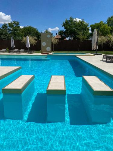 a swimming pool with blue water and benches in it at CasaBlanca vendégház in Abádszalók