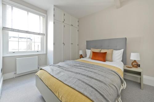 a white bedroom with a large bed with an orange pillow at Fabulous three bedroom flat near Marylebone by UnderTheDoormat in London