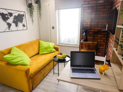 sala de estar con sofá amarillo y mesa con ordenador portátil en Sander Apartments, en Cracovia
