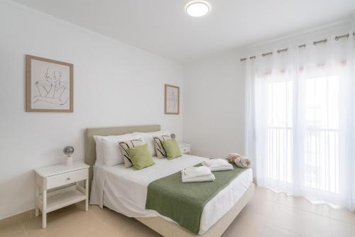 Dormitorio blanco con cama con almohadas verdes en Delightful Cabanas 2 Bedroom apartment en Cabanas de Tavira