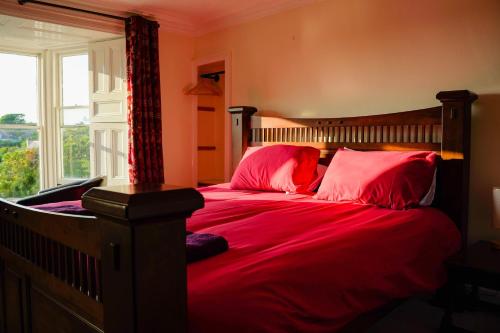 a bedroom with a bed with red sheets and a window at Manorbier House - St Anne's Room in Tenby