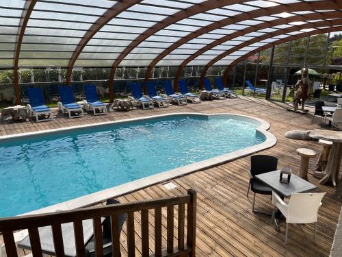 a large swimming pool with chairs and a roof at The Originals Boutique Hôtel Spa Beuzeville Honfleur Sud in Beuzeville