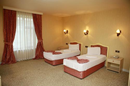 two beds in a hotel room with red curtains at Deluxe Hotel Ganja in Ganja