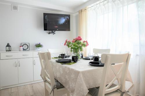 a dining room table with white chairs and a tv on the wall at Apartament Lawenda in Ciechocinek