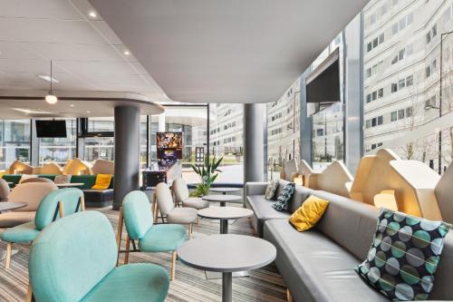a lobby with a couch and tables and chairs at ibis Styles Paris Charles de Gaulle Airport in Roissy-en-France