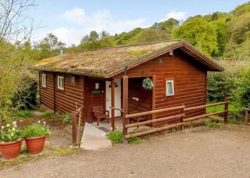 a cabin in the woods with a porch and flowers at Luxury Peak District lodge, hot tub, log burner, nr lake in Rudyard