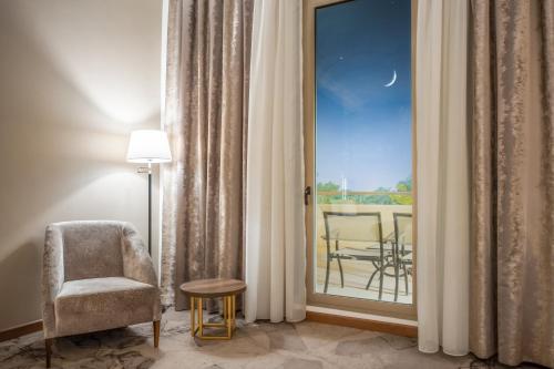 a room with a chair and a window with a balcony at Grand Millennium Al Seef Basra in Al Başrah