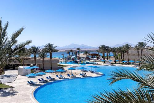 The V Luxury Resort Sahl Hasheesh في الغردقة: حمام سباحة مع المظلات والكراسي الزرقاء والمحيط