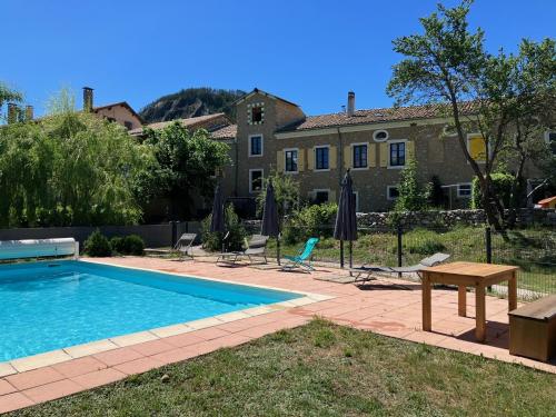 a swimming pool with a table and chairs and a building at La Maison des Hôtes in La Motte-du-Caire