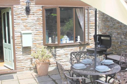 un patio con mesa, sillas y pared de piedra. en Charming 2-Bed Cottage in Modbury en Modbury
