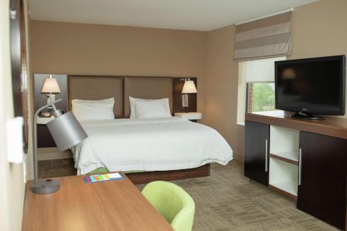 a hotel room with a bed and a flat screen tv at Hampton Inn Commerce/Novi in Walled Lake