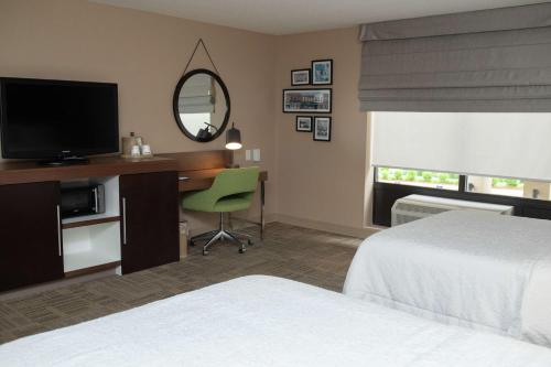 a hotel room with a bed and a desk with a television at Hampton Inn Commerce/Novi in Walled Lake