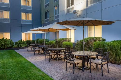 un groupe de tables avec parasols devant un bâtiment dans l'établissement Hilton Garden Inn Islip/MacArthur Airport, à Ronkonkoma