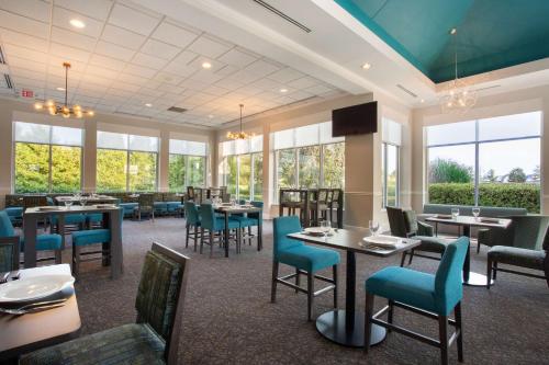 a restaurant with tables and chairs and windows at Hilton Garden Inn Islip/MacArthur Airport in Ronkonkoma