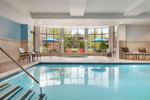 a swimming pool with chairs and tables and windows at Hilton Garden Inn Stony Brook in Stony Brook