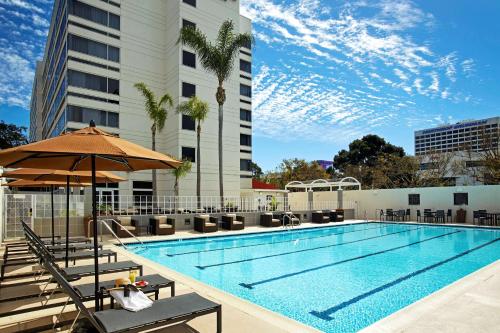 - une piscine avec des chaises et un parasol à côté d'un bâtiment dans l'établissement DoubleTree by Hilton LAX - El Segundo, à El Segundo