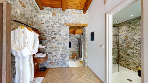 a room with a stone wall with a shower and a robe at Petra Elounda Suites - Adults Only in Elounda